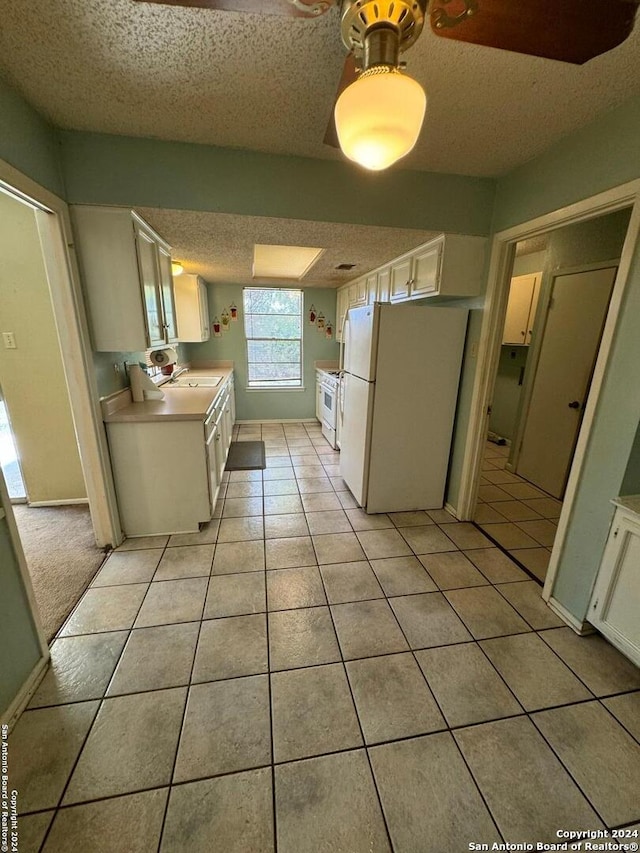 kitchen with white cabinets, a textured ceiling, white appliances, and light tile patterned flooring