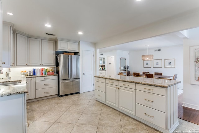 kitchen with decorative light fixtures, stainless steel fridge, light stone counters, and a center island