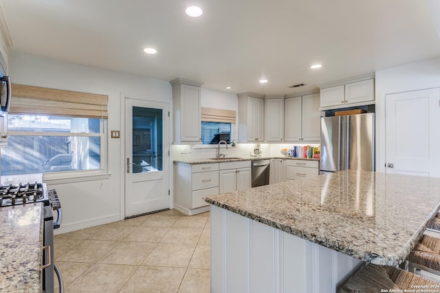 kitchen with sink, white cabinetry, light stone counters, a breakfast bar area, and stainless steel fridge