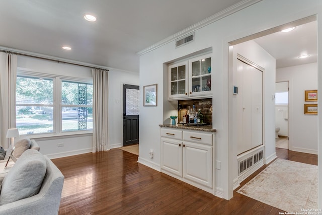 bar featuring white cabinets, ornamental molding, stone counters, and dark wood-type flooring