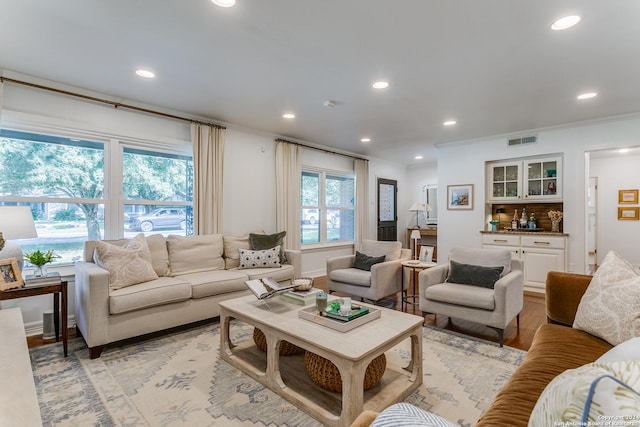 living room with indoor bar, light wood-type flooring, and ornamental molding