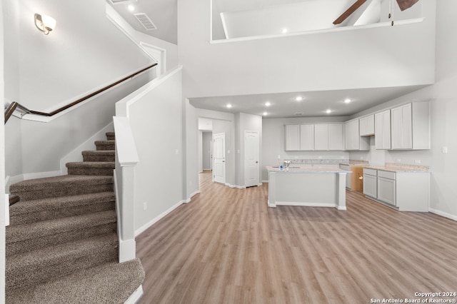 kitchen featuring a kitchen island with sink, ceiling fan, light hardwood / wood-style flooring, a high ceiling, and white cabinetry