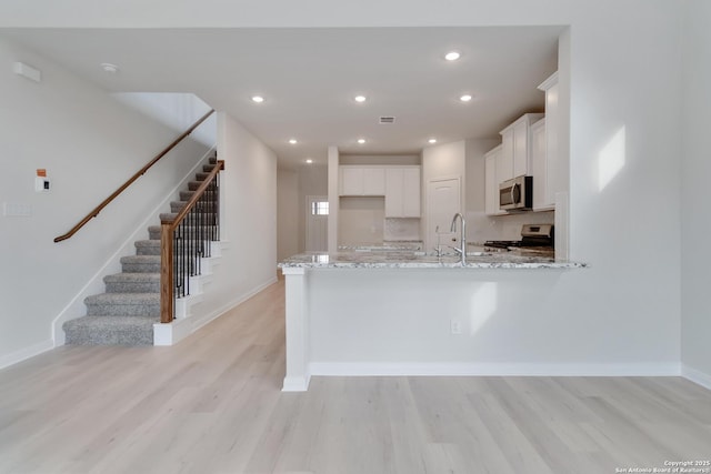 142 Ashley Loop, San Antonio, TX 78253 - kitchen with appliances with stainless steel finishes, white cabinets, light wood finished floors, light stone countertops, and a peninsula