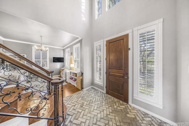 entrance foyer with ornamental molding, a towering ceiling, and an inviting chandelier