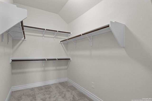 walk in closet with light colored carpet and lofted ceiling