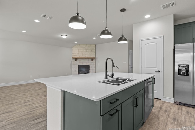 kitchen with appliances with stainless steel finishes, sink, light hardwood / wood-style floors, hanging light fixtures, and an island with sink