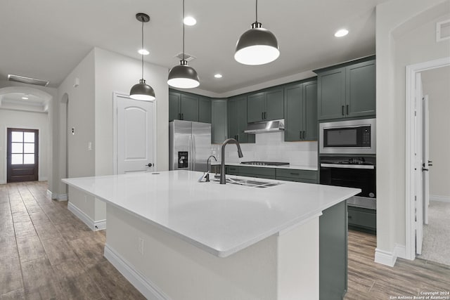 kitchen with stainless steel appliances, hardwood / wood-style floors, an island with sink, decorative light fixtures, and decorative backsplash