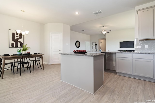 kitchen with light wood-type flooring, light stone counters, ceiling fan with notable chandelier, pendant lighting, and a kitchen island