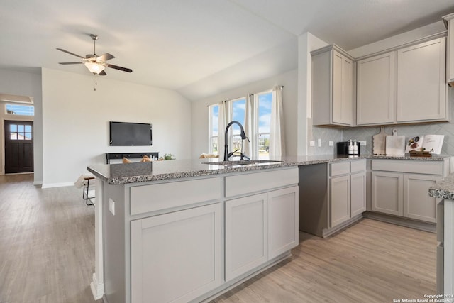 kitchen with kitchen peninsula, backsplash, gray cabinetry, sink, and light hardwood / wood-style floors