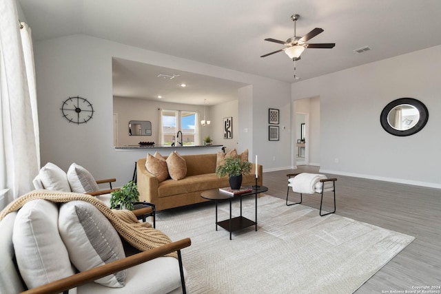 living room with ceiling fan with notable chandelier, light wood-type flooring, lofted ceiling, and sink