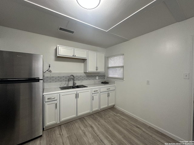 kitchen with stainless steel refrigerator, sink, tasteful backsplash, light hardwood / wood-style flooring, and white cabinets