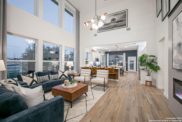 living room with light hardwood / wood-style floors, a high ceiling, and an inviting chandelier