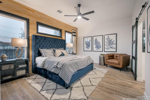 bedroom featuring multiple windows, a barn door, ceiling fan, and wood walls