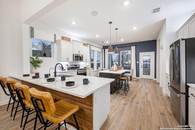 kitchen featuring a breakfast bar, a center island, decorative light fixtures, white cabinetry, and stainless steel appliances