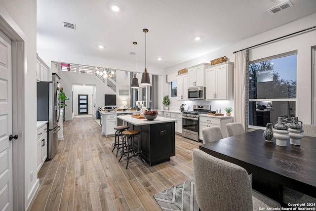 kitchen featuring appliances with stainless steel finishes, decorative light fixtures, a kitchen island, a kitchen bar, and white cabinetry