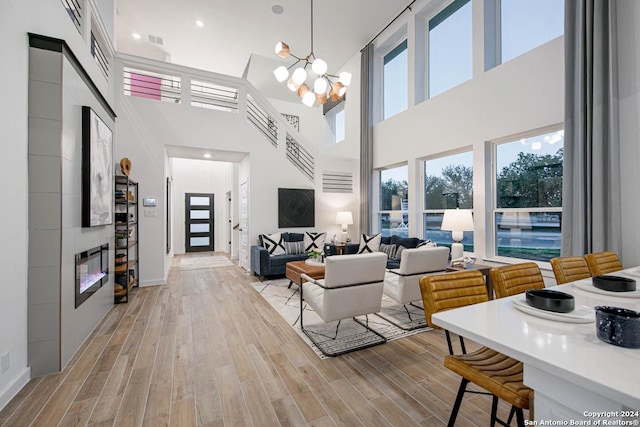 living room featuring a chandelier, a towering ceiling, a fireplace, and light hardwood / wood-style flooring