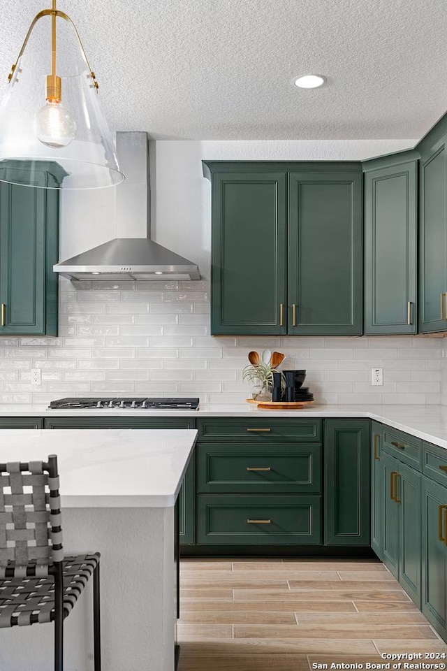 kitchen featuring decorative backsplash, light wood-type flooring, stainless steel gas cooktop, wall chimney range hood, and green cabinets