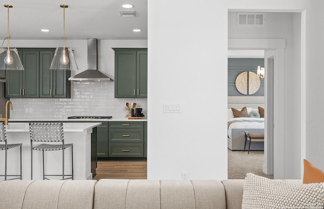 kitchen with pendant lighting, green cabinetry, and wall chimney range hood