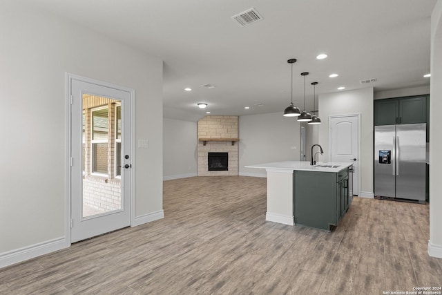 kitchen featuring hanging light fixtures, stainless steel fridge, wood-type flooring, a kitchen island with sink, and a fireplace