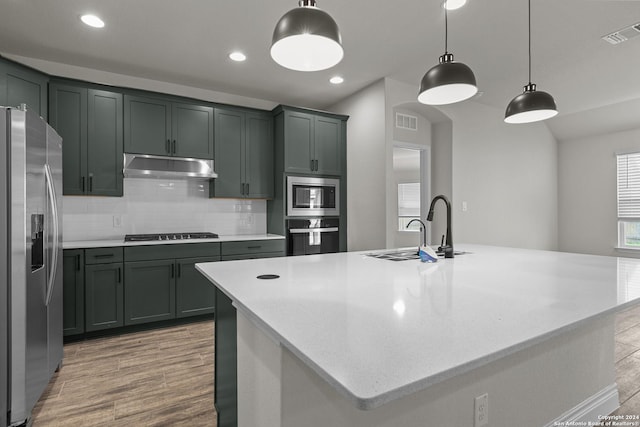 kitchen with light wood-type flooring, stainless steel appliances, a spacious island, sink, and pendant lighting