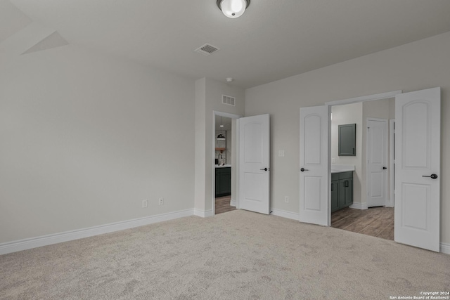 unfurnished bedroom featuring light colored carpet and connected bathroom