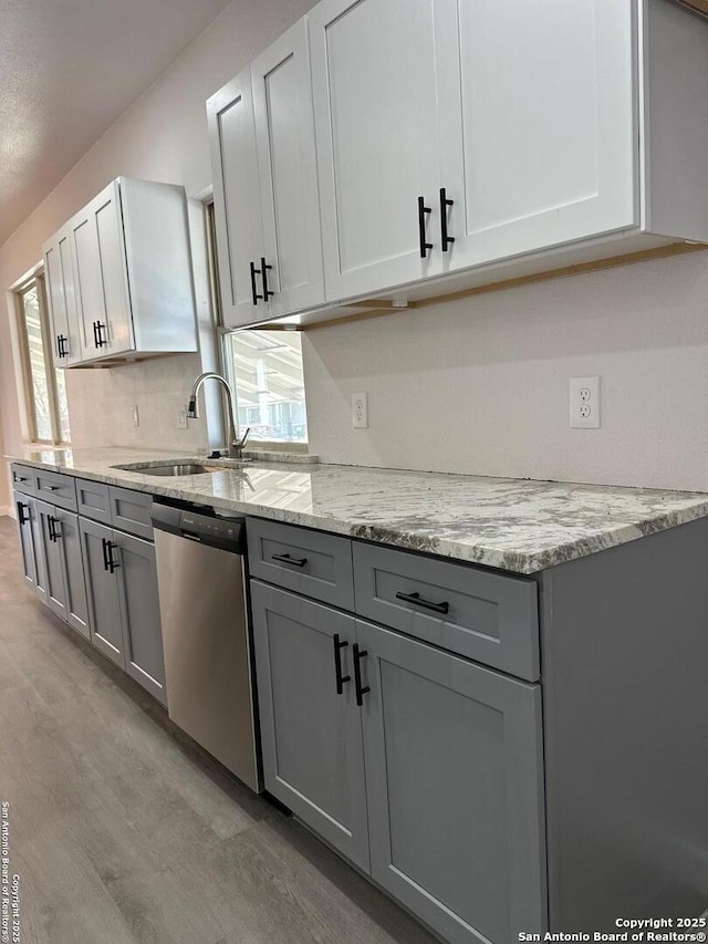 kitchen featuring sink, dishwasher, light stone counters, light wood-type flooring, and gray cabinets