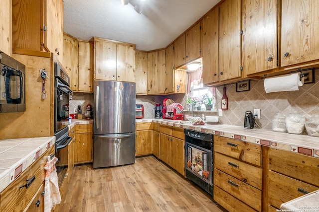 kitchen featuring tile countertops, stainless steel fridge, light hardwood / wood-style floors, and decorative backsplash