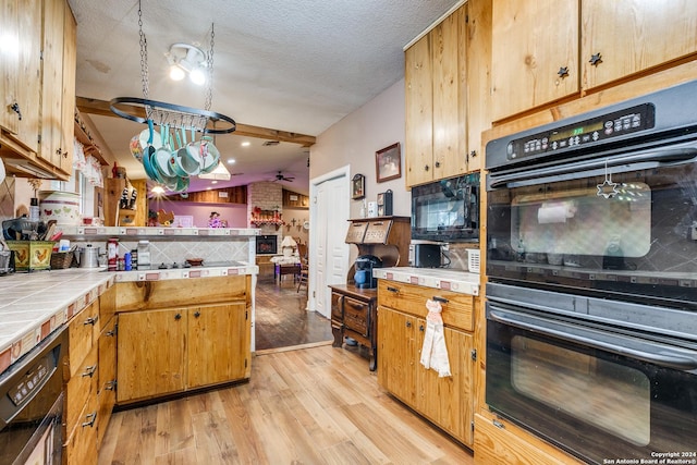 kitchen with tile counters, vaulted ceiling, light wood-type flooring, and tasteful backsplash