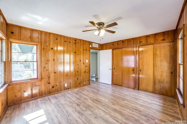 unfurnished bedroom with light hardwood / wood-style flooring, ceiling fan, and wood walls