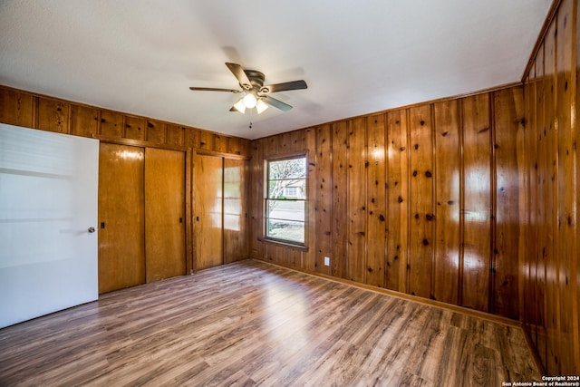 unfurnished bedroom featuring hardwood / wood-style flooring, ceiling fan, and wood walls