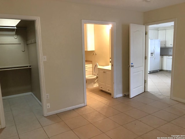 unfurnished bedroom with ensuite bath, a walk in closet, white fridge with ice dispenser, and light tile patterned flooring