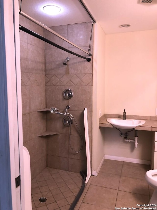 bathroom with tile patterned floors, sink, a tile shower, and toilet