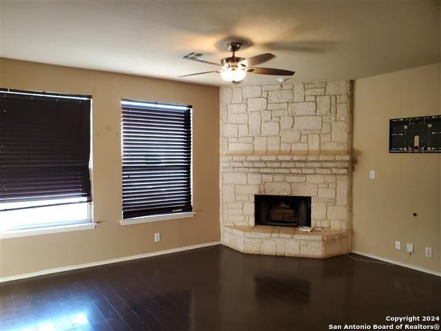 unfurnished living room with a stone fireplace, ceiling fan, and dark wood-type flooring