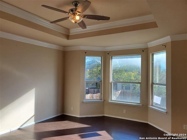 unfurnished room featuring a tray ceiling, ceiling fan, dark hardwood / wood-style floors, and ornamental molding