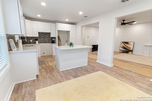 kitchen with white cabinetry, a center island, sink, light hardwood / wood-style floors, and decorative backsplash