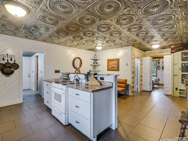 kitchen featuring wooden walls, white gas stove, white cabinets, and dark stone counters