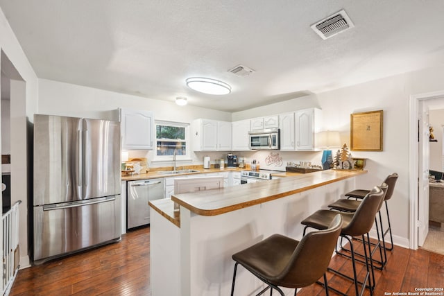 kitchen with white cabinetry, stainless steel appliances, dark hardwood / wood-style floors, kitchen peninsula, and a kitchen bar