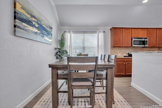 dining space with crown molding, light hardwood / wood-style flooring, and lofted ceiling