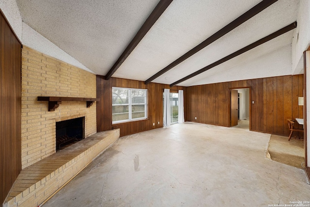 unfurnished living room with wooden walls, a fireplace, lofted ceiling with beams, and a textured ceiling