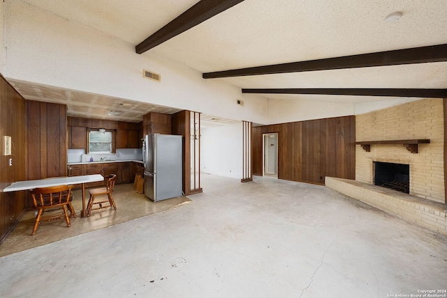 unfurnished living room featuring sink, a brick fireplace, vaulted ceiling with beams, a textured ceiling, and wooden walls