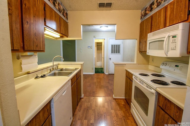 kitchen featuring kitchen peninsula, light wood-type flooring, a textured ceiling, white appliances, and sink