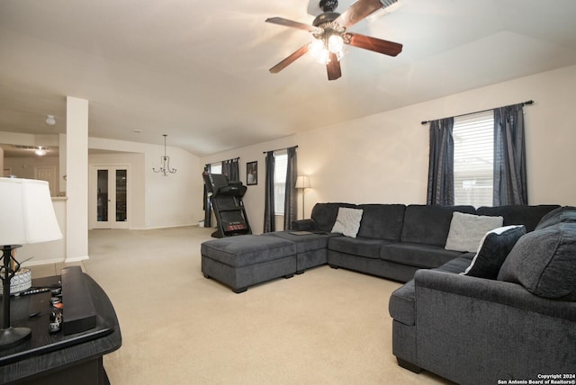 carpeted living room with ceiling fan with notable chandelier and vaulted ceiling