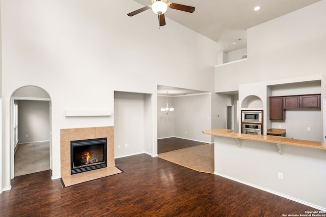 unfurnished living room featuring ceiling fan with notable chandelier, dark hardwood / wood-style flooring, high vaulted ceiling, and a tiled fireplace