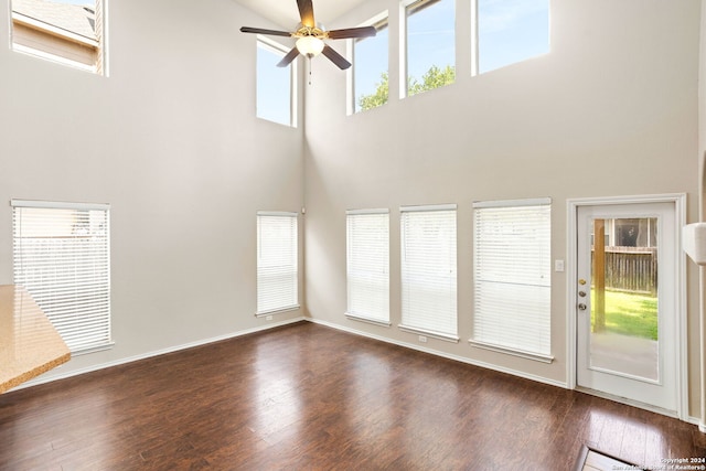 unfurnished living room featuring ceiling fan, a towering ceiling, and dark wood-type flooring