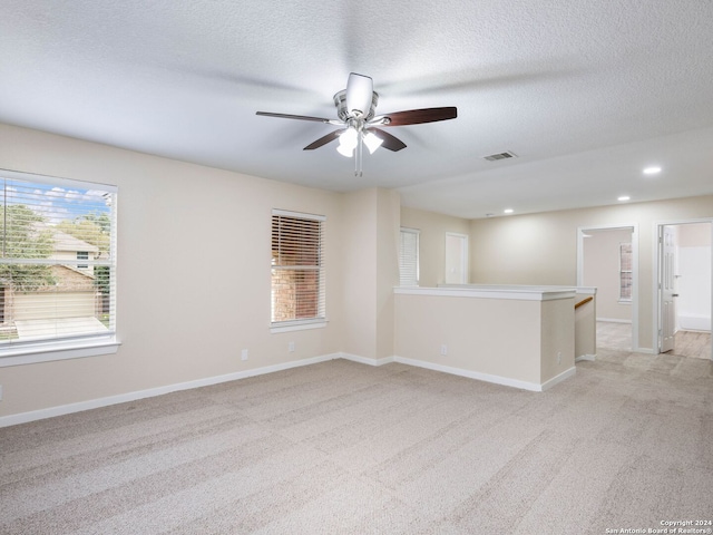 carpeted empty room with a textured ceiling, ceiling fan, and a healthy amount of sunlight