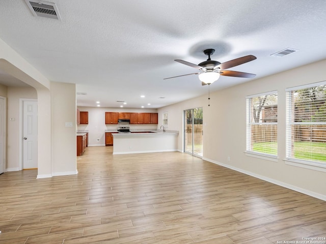 unfurnished living room featuring ceiling fan, light hardwood / wood-style floors, and a textured ceiling