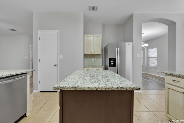 kitchen with light stone countertops, appliances with stainless steel finishes, cream cabinetry, a kitchen island, and light wood-type flooring