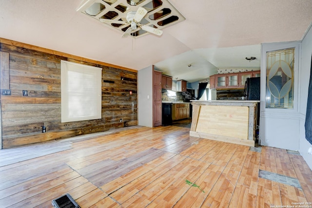 kitchen with light wood-type flooring, vaulted ceiling, ceiling fan, black appliances, and wood walls