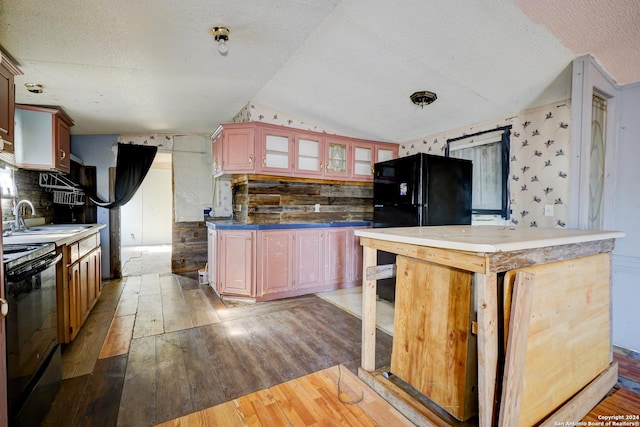 kitchen with a textured ceiling, vaulted ceiling, sink, black appliances, and hardwood / wood-style floors