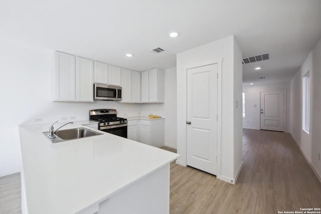 kitchen with white cabinets, sink, light hardwood / wood-style floors, kitchen peninsula, and stainless steel appliances